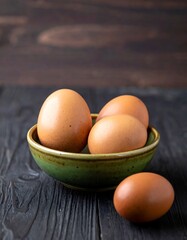 Fresh brown eggs in a green bowl on a wooden table surface