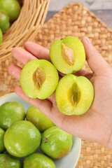 Fresh Green Plums Cut in Half Held in Hand with Whole Fruits Display