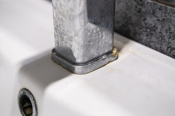 A dirty metal faucet in the sink with limescale, rust marks, and grime around the mixer, showing neglect and the need for cleaning.