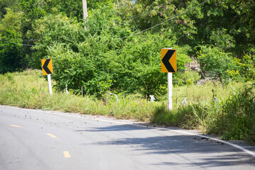 Country road with sharp turn signs surrounded by lush green vegetation and trees in a rural setting