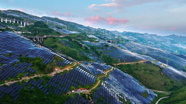 Aerial shot of a large solar farm with photovoltaic panels covering the green mountain slopes, generating clean and renewable electricity.