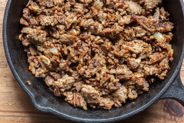 Beef mince with onion fried in a cast iron frying pan. On a wooden board background backdrop.