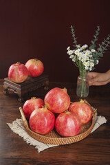 Fresh Red Pomegranates in Wicker Basket Still Life with White Flowers on Rustic Wood Table