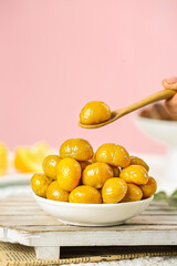 Fresh Golden Chestnuts in Bowl with Wooden Spoon on Pink Background