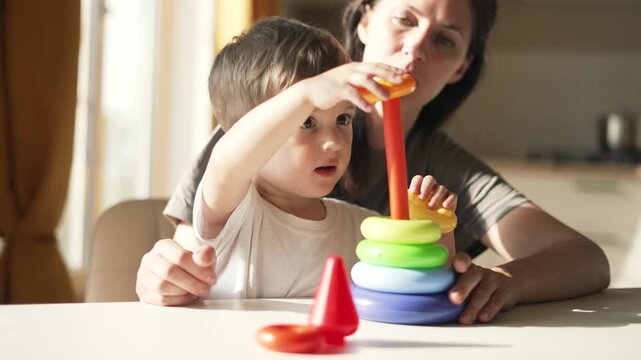 Child stacking toy with mother guiding toddler and parent hands during home play learning activity using colorful stacker ring for toy development and concentration and fine motor skill practice
