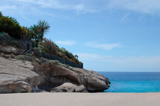 Tropical beach with a cliff face covered in lush vegetation and palm trees, meeting the crystal-clear turquoise ocean. A private paradise, a hidden gem.