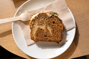 Close-up of a slice of pumpkin cake on a white plate with a wooden fork, served on a wooden cafe table.