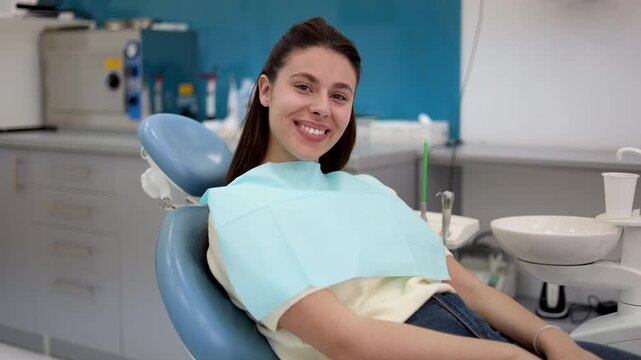 Smiling young woman in a dental chair, awaiting a check-up in a contemporary clinic, exudes satisfaction