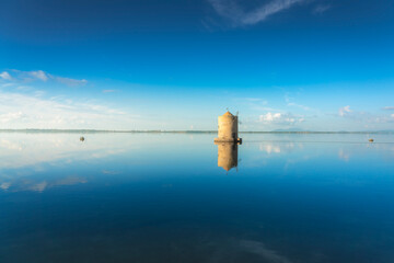 Old spanish windmill reflected in Orbetello lagoon waters, Argentario, Italy.