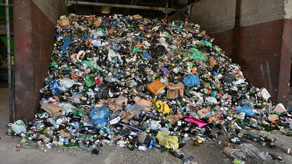 Large pile of mixed waste including bottles, plastic bags, and other garbage, collected inside a recycling facility, illustrating waste management challenges