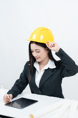 A studio shot portrays an Asian female engineer who owns a company, sitting at her desk in the industry setting with a laptop and greenprint, highlighting business success and leadership.