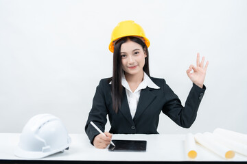 An Asian female engineer in suit is portrayed in a studio shot, seated at her desk with a tablet...