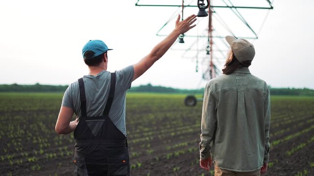 Inspecting irrigation pivot and crop growth in planted field with two farmer and worker walking rows checking plant and soil condition during agriculture inspection under pivot irrigation system