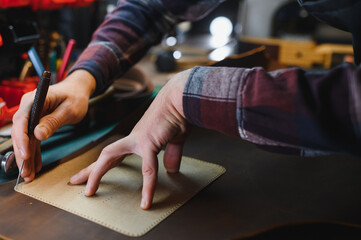 Man working with leather. Professional makes a wallet.