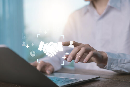 Businessman using a laptop with a handshake icon, symbolizing partnership, agreement, trust, teamwork, and successful business collaboration in digital communication and corporate networking.