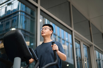 Asian man exercises on an elliptical machine.