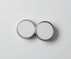 Two blank round metal containers sit side-by-side on a clean white surface