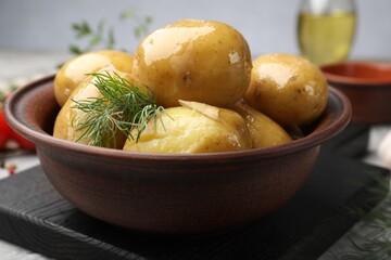 Tasty young boiled potatoes with dill and oil in bowl on grey table, closeup
