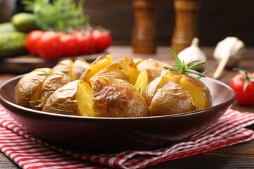 Tasty baked potatoes with rosemary served on wooden table, closeup