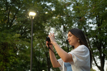 Young woman taking photos in the park with a mirrorless retro camera