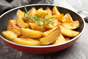 Tasty baked potatoes with rosemary in frying pan on grey textured table, closeup