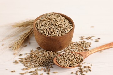Rye grains in bowl, spoon and spikes on white wooden table, closeup