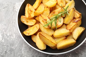 Tasty baked potatoes with rosemary in frying pan on grey textured table, top view
