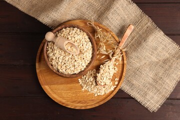 Oat flakes in bowl, scoop, spoon and florets on wooden table, flat lay