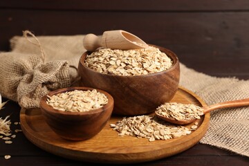 Oat flakes in bowls, scoop, spoon and florets on wooden table, closeup