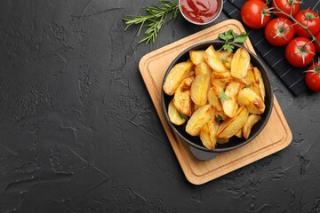 Tasty baked potatoes in frying pan on dark textured table, flat lay. Space for text