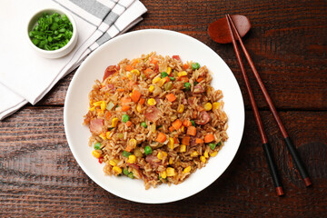 Tasty fried rice and chopsticks on wooden table, flat lay