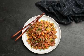 Delicious fried rice with vegetables and chopsticks on grey textured table, top view