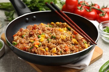 Delicious fried rice in frying pan and chopsticks on grey table, closeup