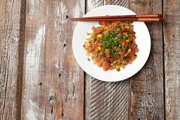 Delicious fried rice with vegetables and chopsticks on wooden table, top view. Space for text