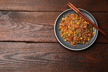 Delicious fried rice with vegetables and chopsticks on wooden table, top view. Space for text