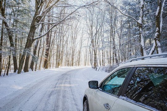 White SUV driving along woodland country road on a snowy winter day