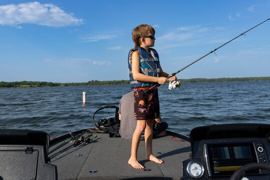 Boy in lifejacket holding fishing  rod on a  boat on the lake