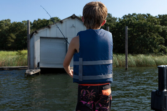 Boy fishing near a dockside boathouse on a sunny lake day