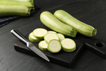 Fresh ripe zucchinis with knife on black textured table. Whole and cut