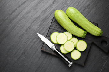 Fresh ripe zucchinis with knife on black textured table, top view. Space for text