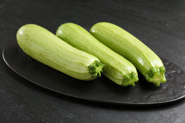 Fresh ripe zucchinis on black textured table, closeup