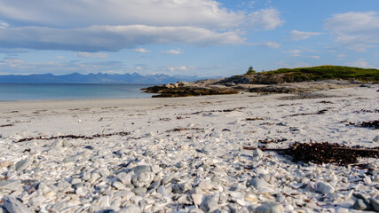 Serene rocky beach in Bognes, Lofoten, Norway, featuring smooth pebbles and gentle waves under a clear blue sky. Nearby mountains complete this picturesque coastal view, ideal for nature lovers.