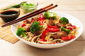Delicious noodles with meat and vegetables served on light wooden table, closeup