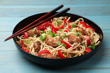 Tasty noodles with chicken, green onions and vegetables served on blue wooden table, closeup