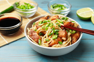 Tasty noodles with chicken, green peppers and sesame seeds served on blue wooden table, closeup