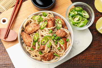 Tasty noodles with chicken, green peppers and sesame seeds served on wooden table, flat lay