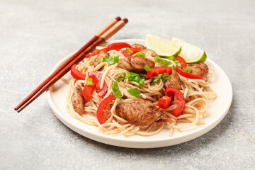 Tasty noodles with chicken, green onions and vegetables served on light grey table, closeup