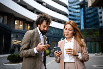 Businesspeople using smartphone and discussing during coffee break outdoors