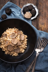 Black truffle risotto recipe. Autumn creamy consistency risotto in stylish black dish on the black background. Dark autumn or winter mood in the style of the Chef's table, close up