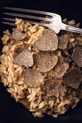 Black truffle risotto recipe. Autumn creamy consistency risotto in stylish black dish on the black background. Dark autumn or winter mood in the style of the Chef's table, close up